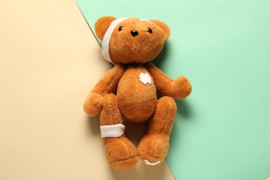 Photo of Teddy bear with bandages and sticking plasters on color background, top view