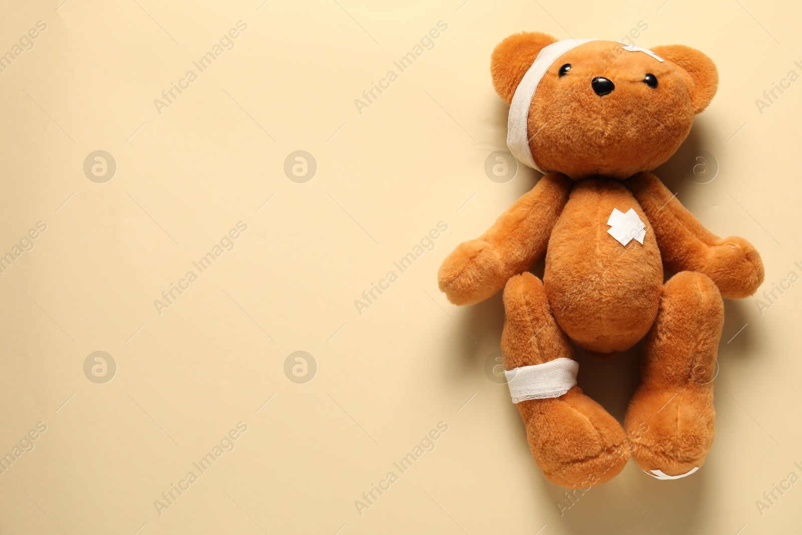 Photo of Teddy bear with bandages and sticking plasters on beige background, top view. Space for text