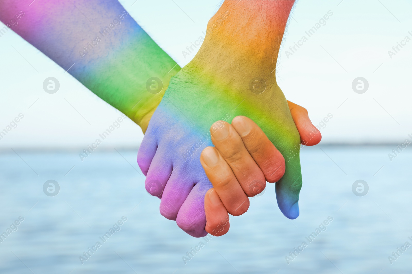 Image of Gay couple holding hands near river, closeup. Toned in LGBT colors. Tolerance and acceptance