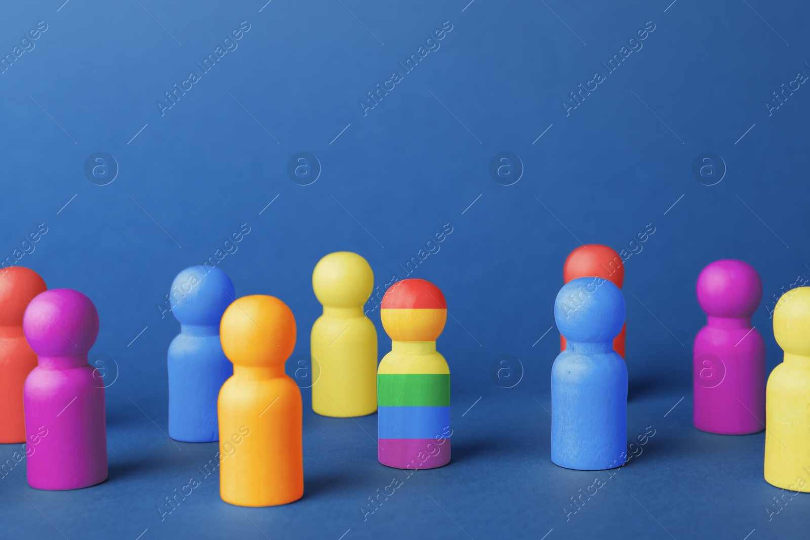 Image of One wooden figure in LGBT colors among others on blue background. Tolerance and acceptance