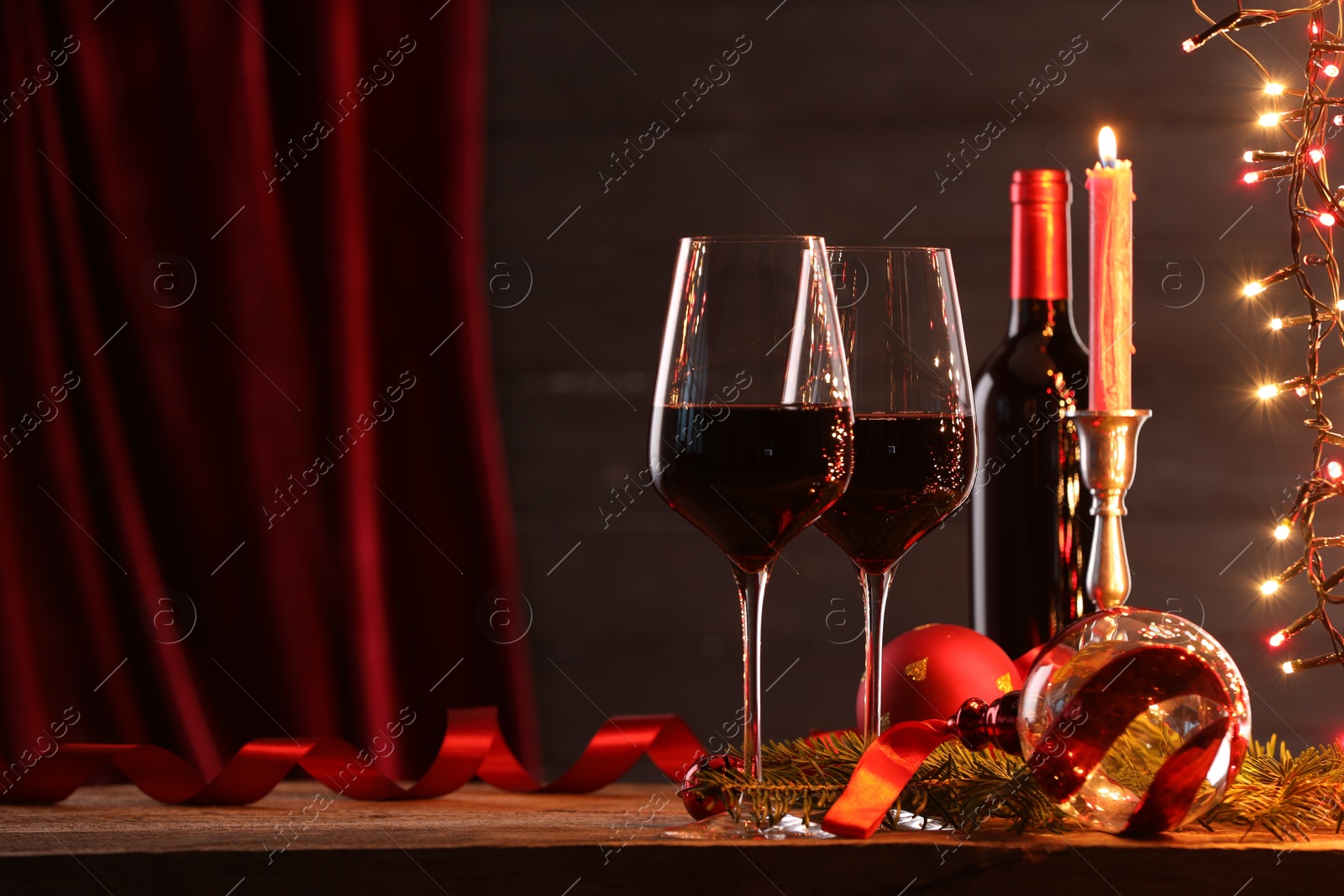 Photo of Red wine, Christmas lights and ornaments on wooden table. Space for text