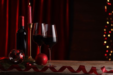 Photo of Red wine, Christmas ornaments and fir branch on wooden table against blurred festive lights. Space for text