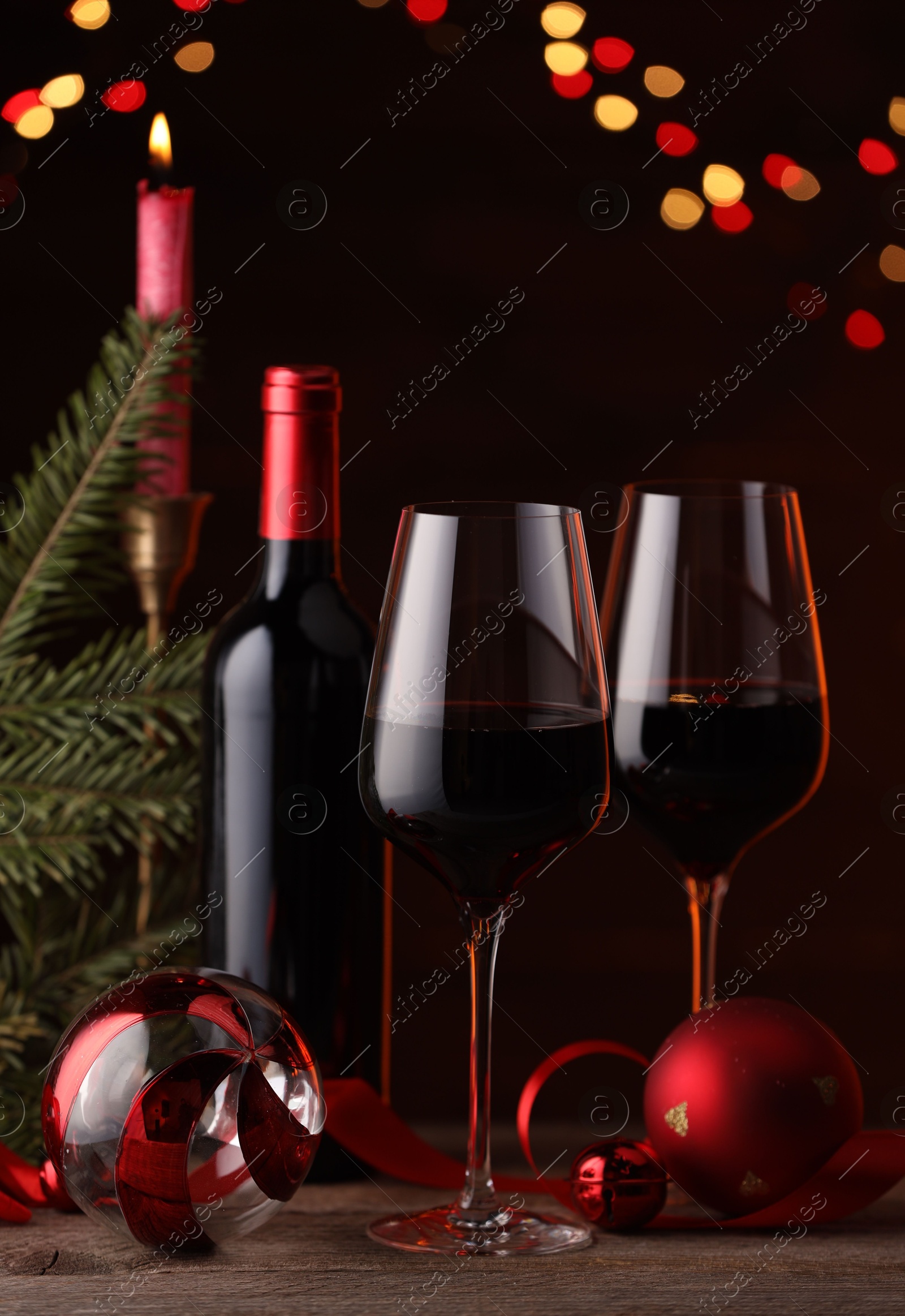 Photo of Red wine, Christmas ornaments and fir branch on wooden table against blurred festive lights