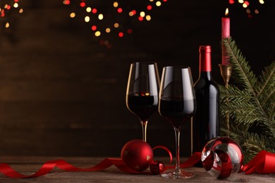 Photo of Red wine, Christmas ornaments and fir branch on wooden table against blurred festive lights. Space for text