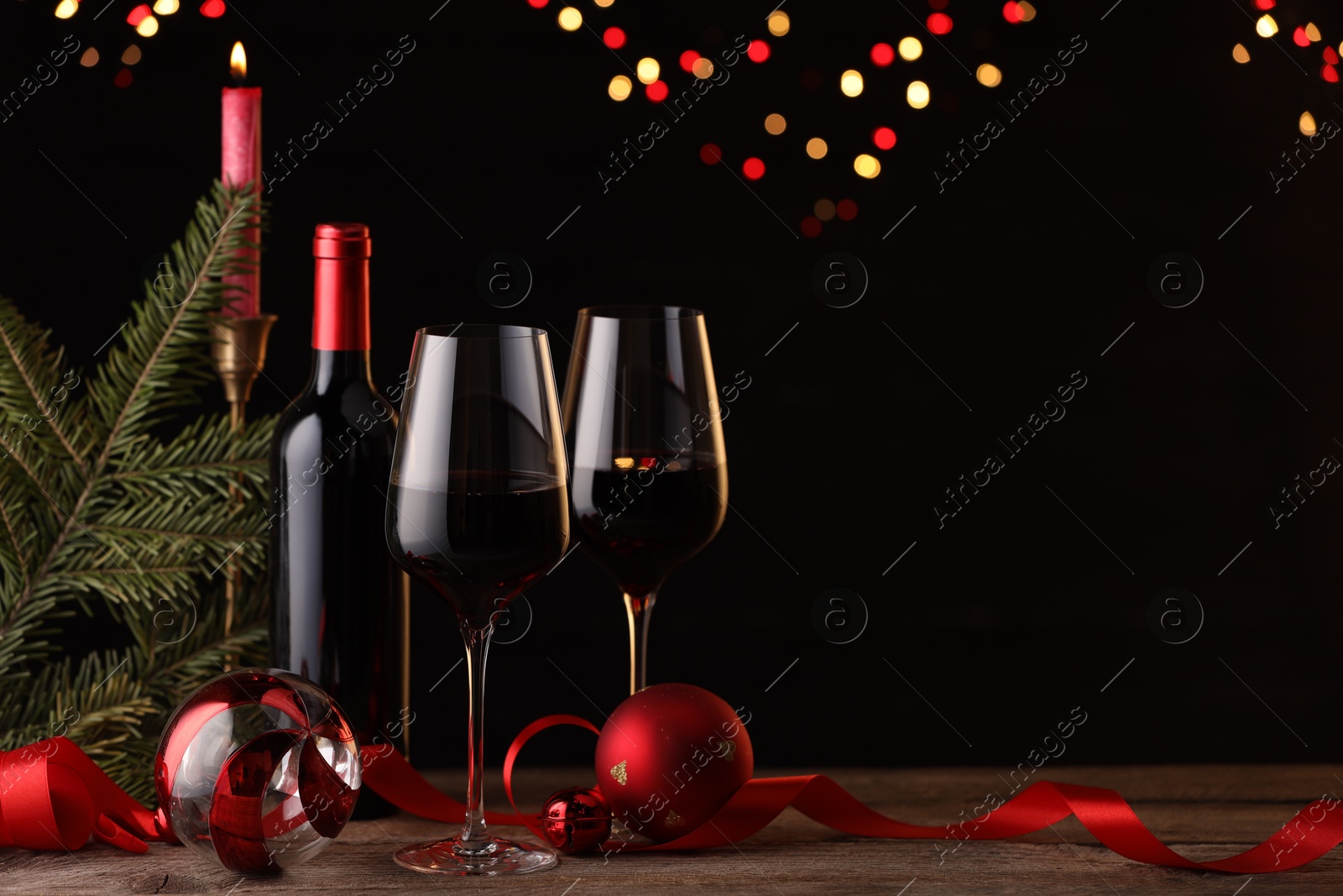 Photo of Red wine, Christmas ornaments and fir branch on wooden table against blurred festive lights. Space for text