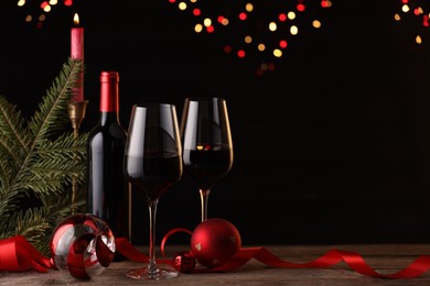 Photo of Red wine, Christmas ornaments and fir branch on wooden table against blurred festive lights. Space for text