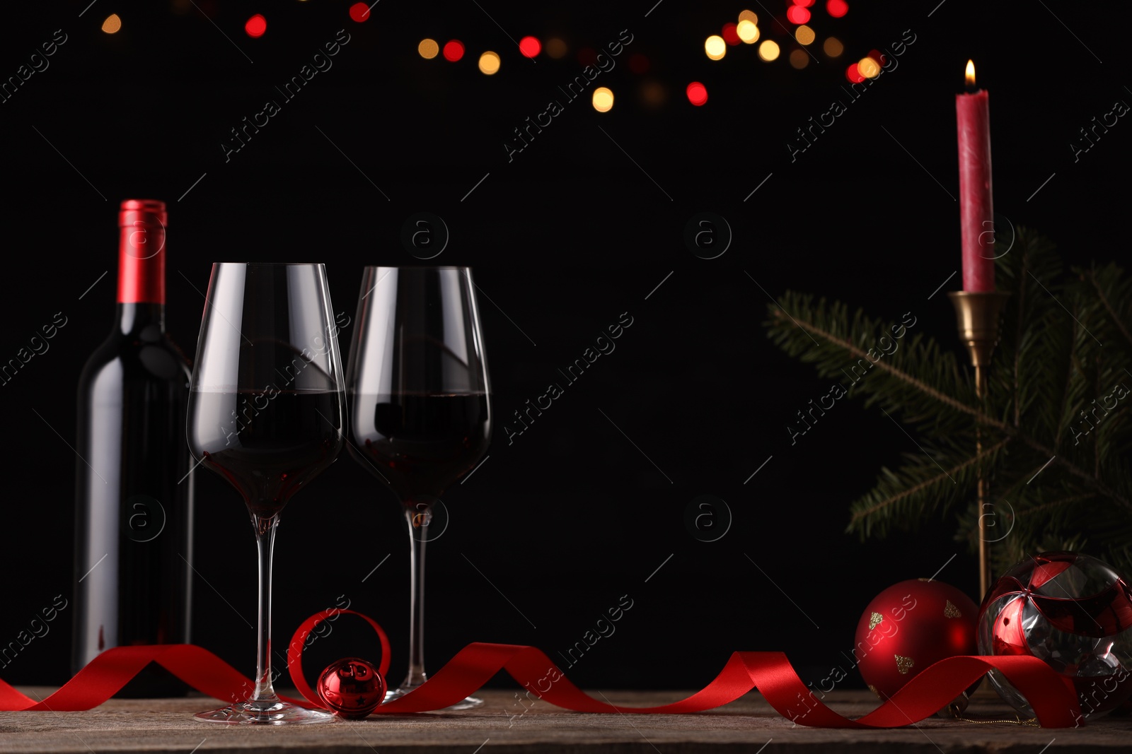 Photo of Red wine, Christmas ornaments and fir branch on wooden table against blurred festive lights