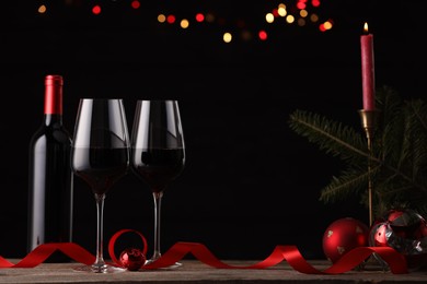 Photo of Red wine, Christmas ornaments and fir branch on wooden table against blurred festive lights