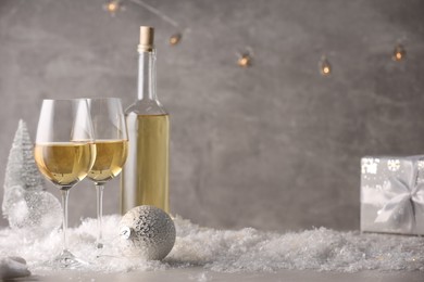 Photo of White wine, Christmas decor and artificial snow on light grey background. Space for text