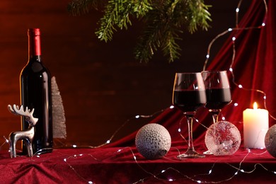 Photo of Red wine, Christmas lights and ornaments on table. Space for text