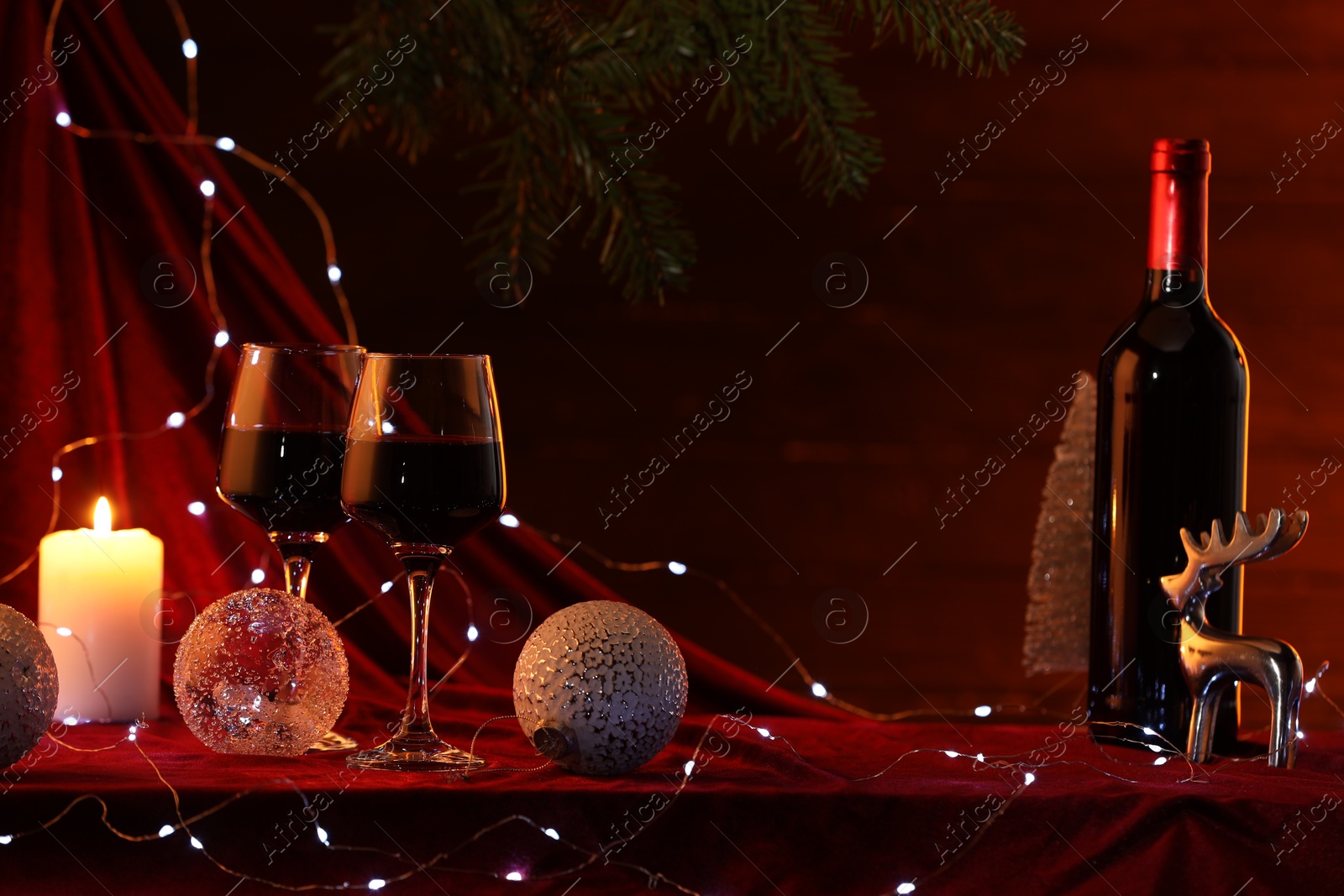 Photo of Red wine, Christmas lights and ornaments on table. Space for text