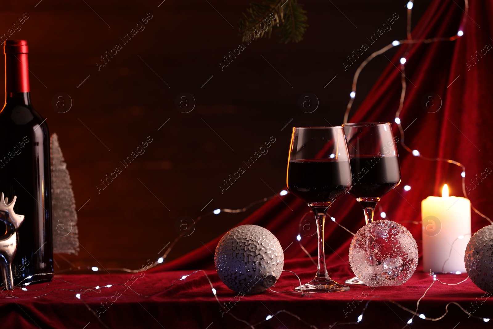 Photo of Red wine, Christmas lights and ornaments on table. Space for text