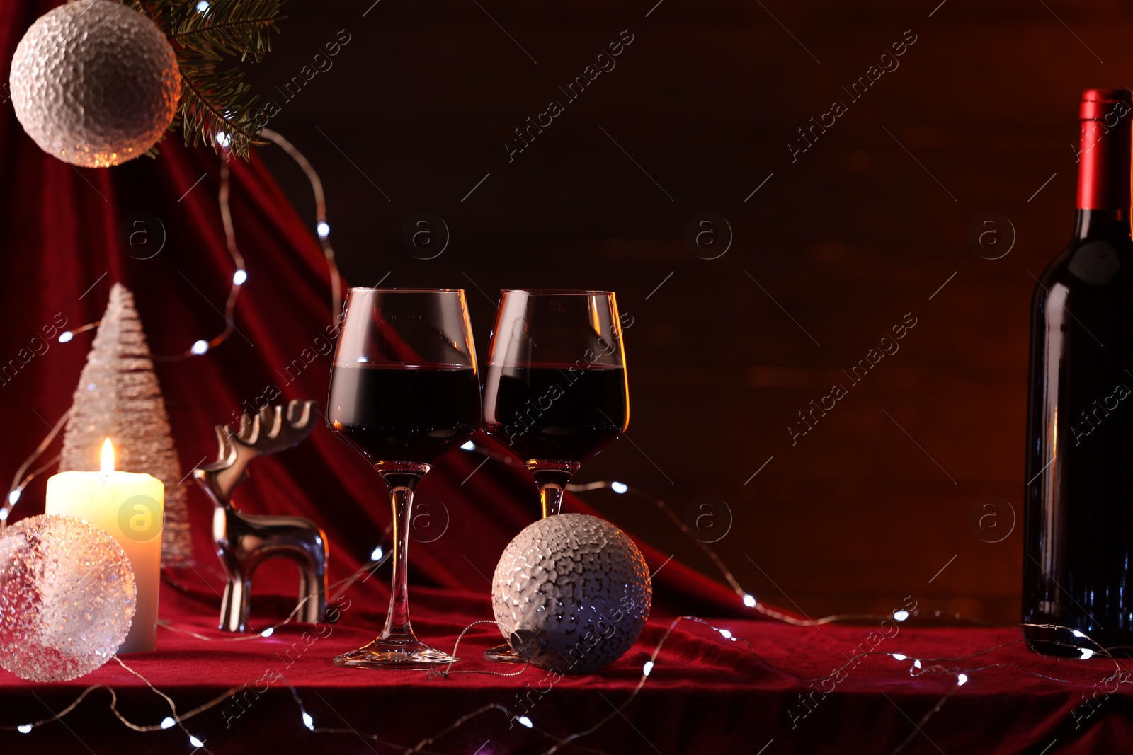 Photo of Red wine, Christmas lights and ornaments on table. Space for text