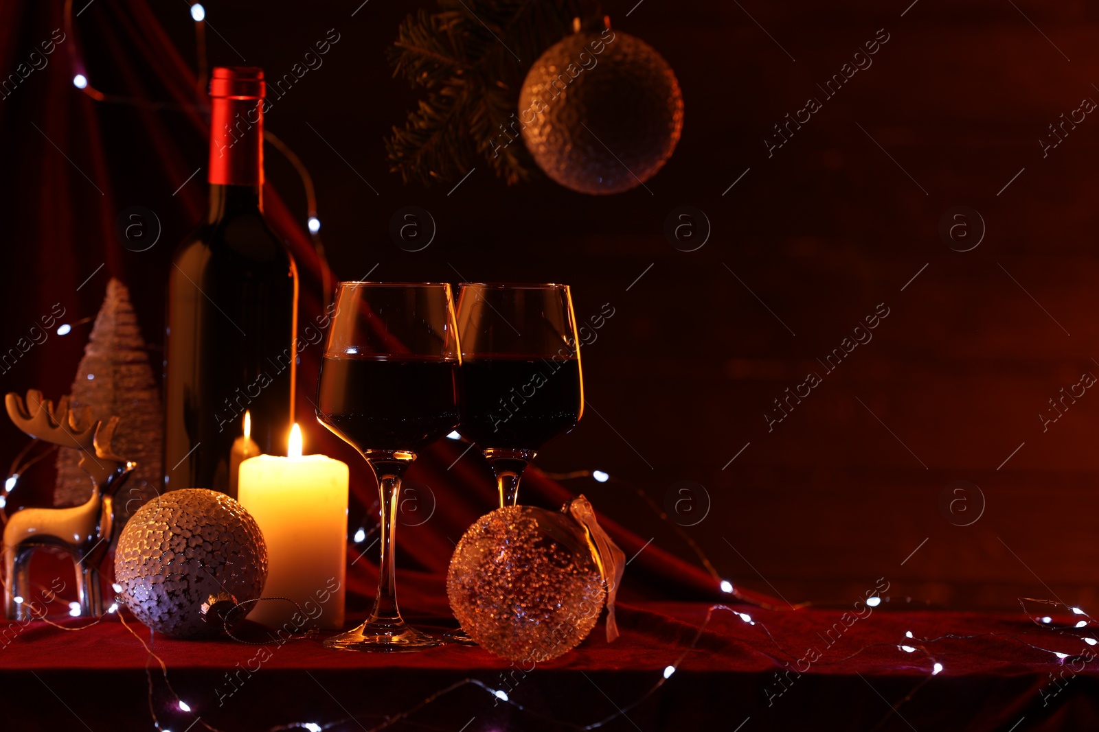 Photo of Red wine, Christmas lights and ornaments on table. Space for text