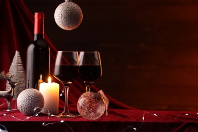 Photo of Red wine, Christmas lights and ornaments on table. Space for text