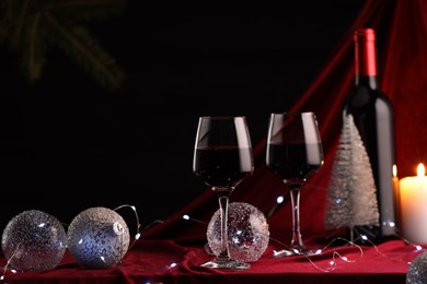 Photo of Red wine, Christmas lights and ornaments on table. Space for text