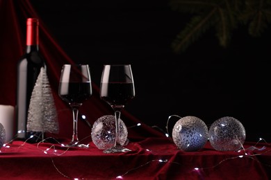 Photo of Red wine, Christmas lights and ornaments on table. Space for text