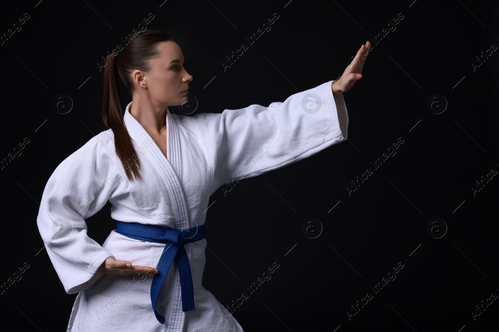 Photo of Young woman in kimono practicing karate on black background