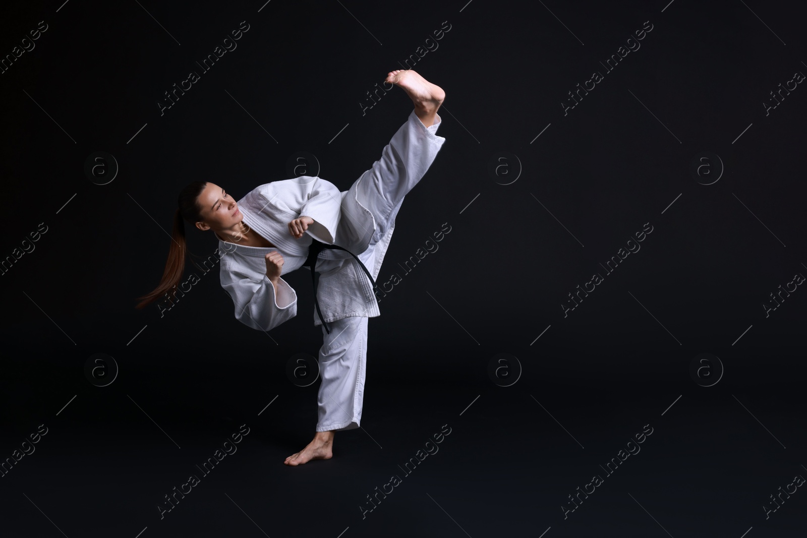 Photo of Young woman in kimono practicing karate on black background, space for text