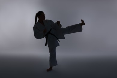 Photo of Silhouette of woman in kimono practicing karate on light background