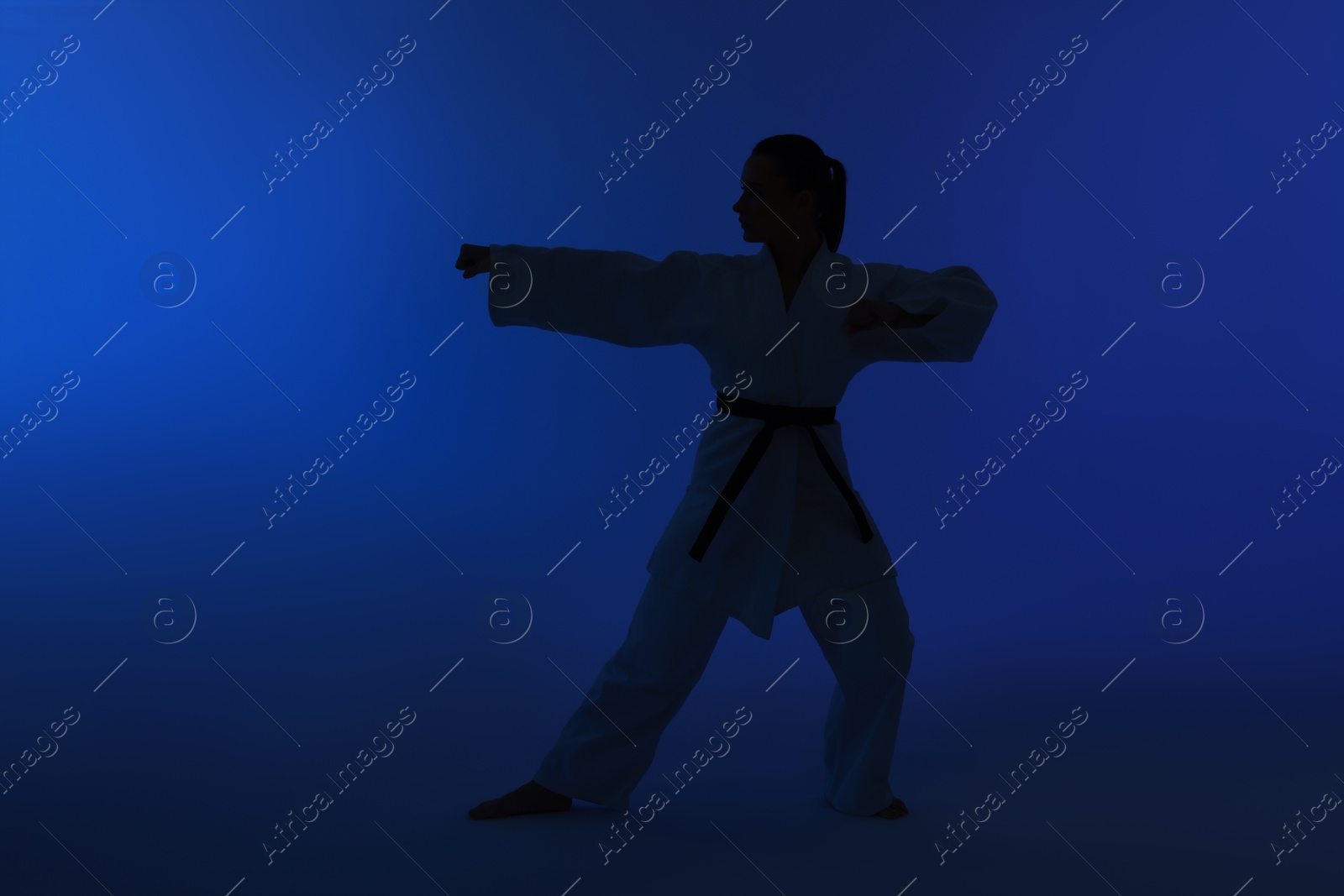 Photo of Silhouette of woman in kimono practicing karate on dark blue background