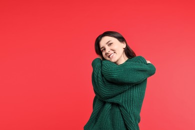 Beautiful young woman hugging herself on red background, space for text