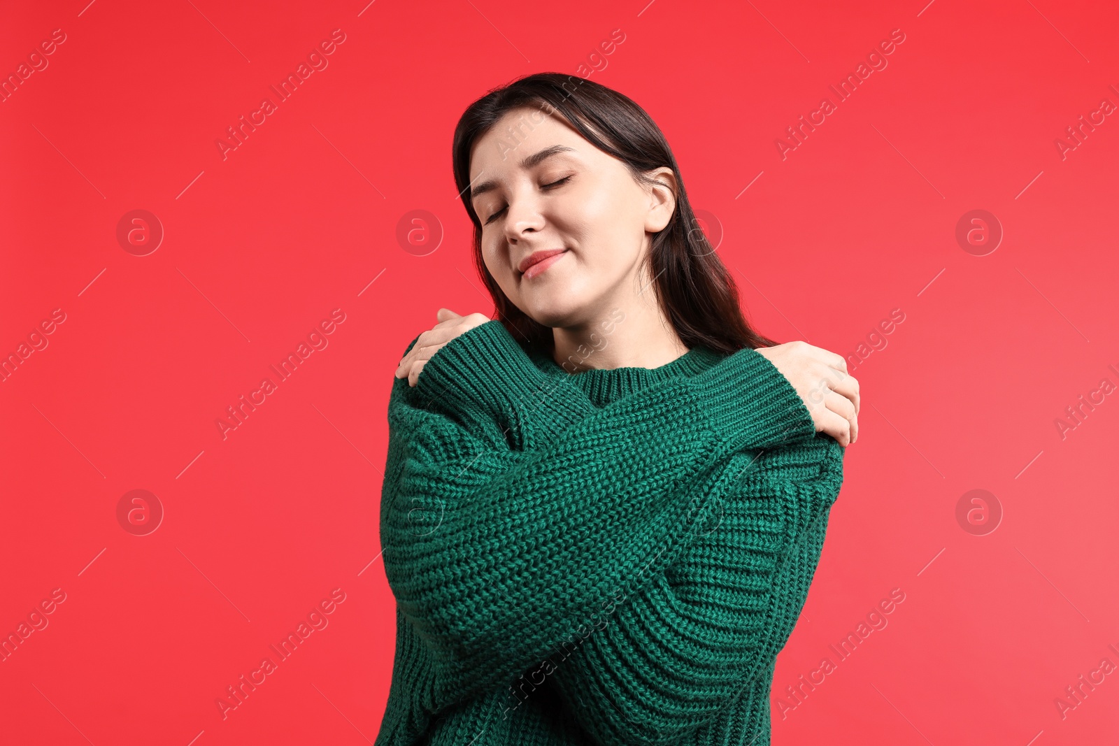 Photo of Beautiful young woman hugging herself on red background