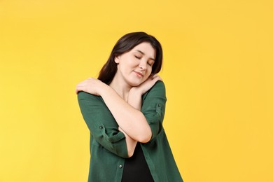 Beautiful young woman hugging herself on yellow background