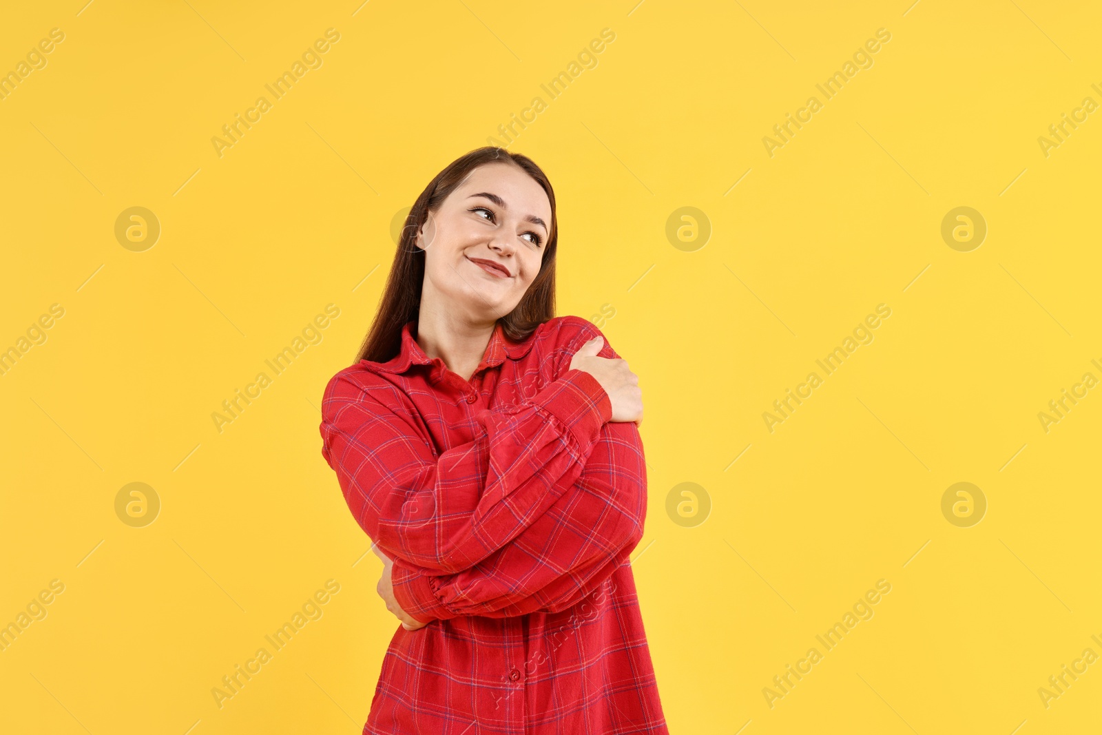 Photo of Beautiful young woman hugging herself on yellow background