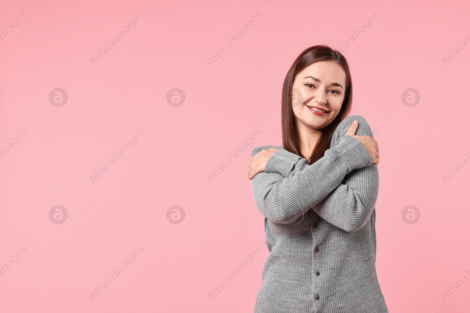 Photo of Beautiful young woman hugging herself on pink background, space for text