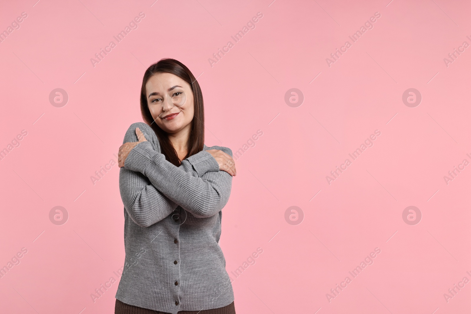 Photo of Beautiful young woman hugging herself on pink background, space for text