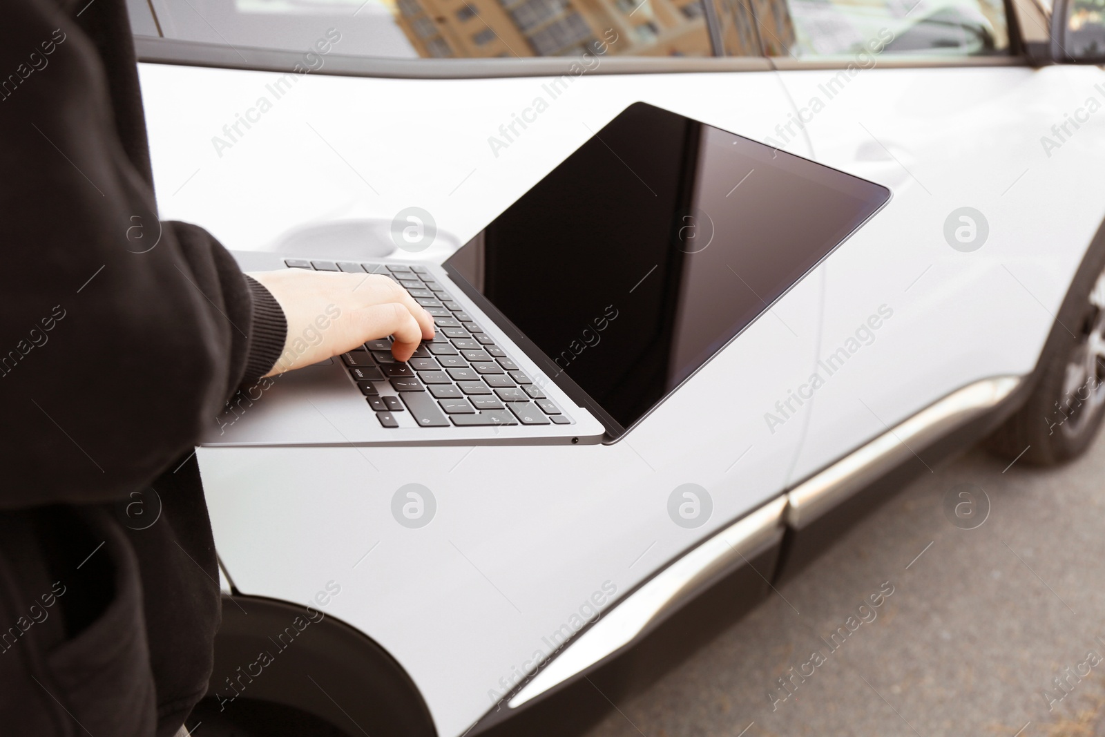 Photo of Thief hacking car system with laptop near vehicle, closeup