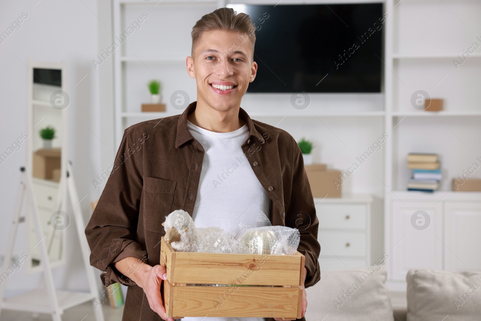 Photo of Happy man holding wooden crate with stuff in new apartment. Housewarming party