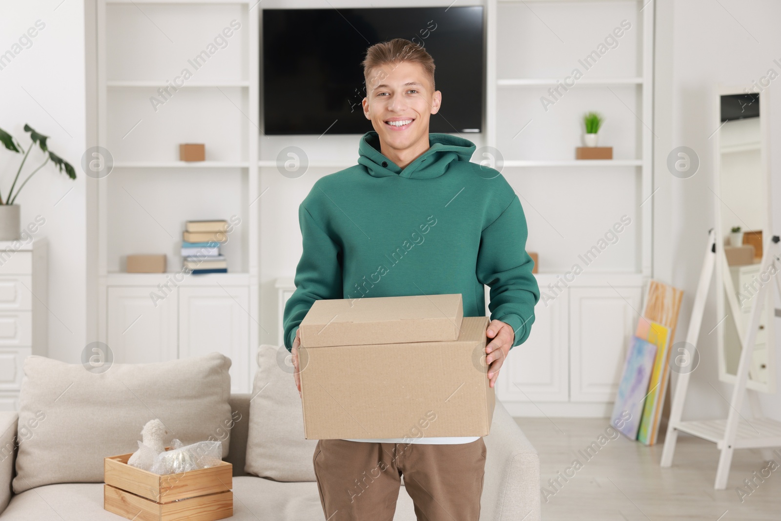 Photo of Happy man with moving boxes in new apartment. Housewarming party