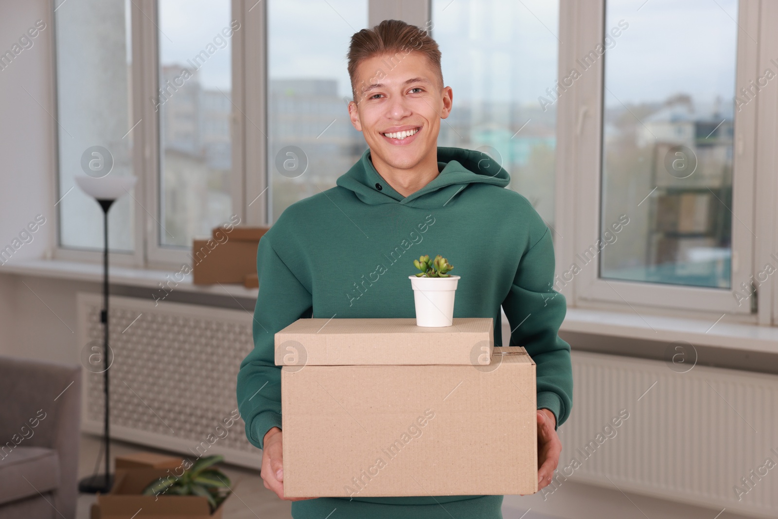 Photo of Happy man with moving boxes and houseplant in new apartment. Housewarming party