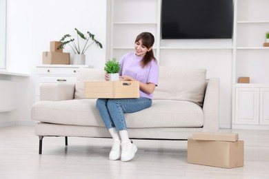 Happy woman holding wooden crate with stuff on sofa in new apartment. Housewarming party