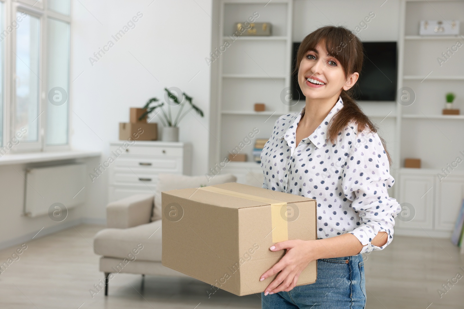 Photo of Happy woman with moving box in new apartment. Housewarming party