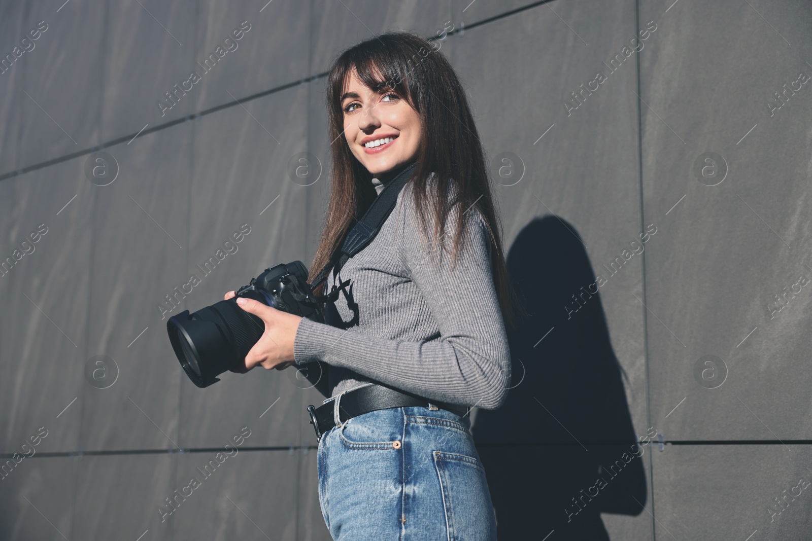 Photo of Professional photographer with digital camera near grey wall outdoors