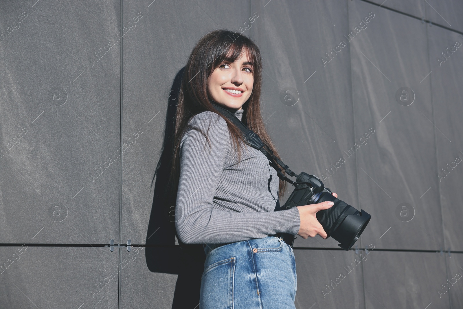 Photo of Professional photographer with digital camera near grey wall outdoors