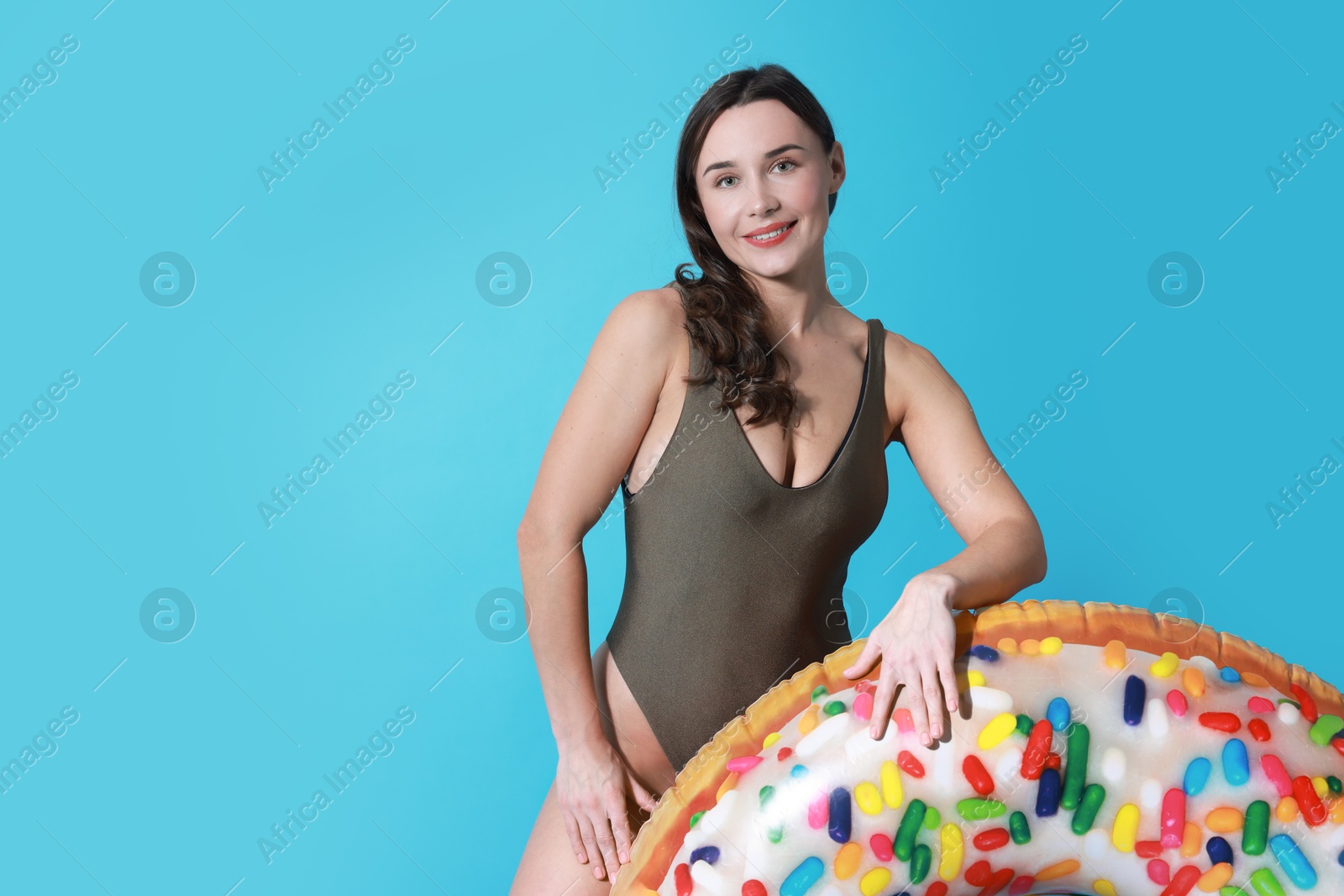 Photo of Beautiful woman in swimsuit with inflatable ring on light blue background. Space for text