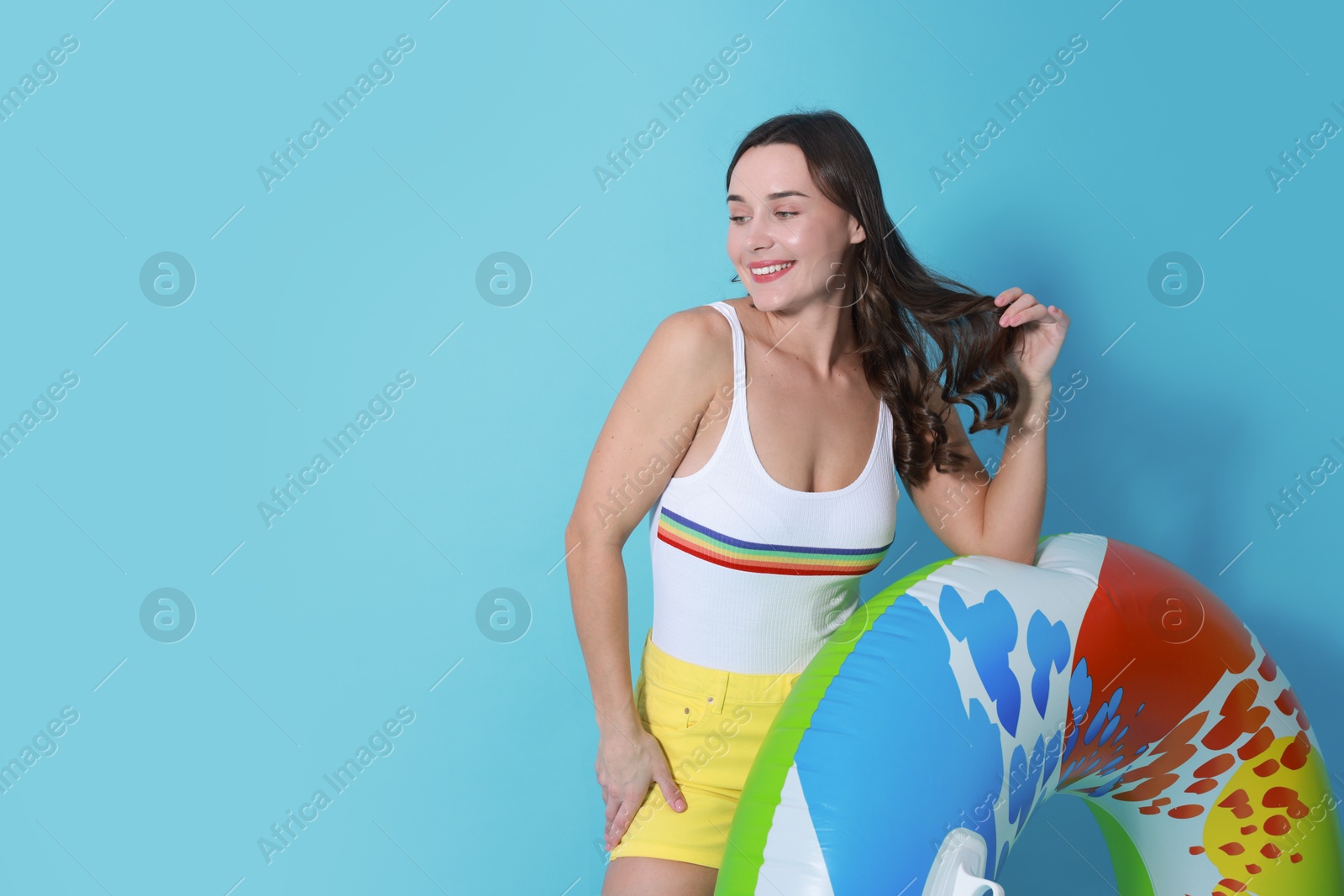 Photo of Beautiful woman in swimsuit with inflatable ring on light blue background. Space for text