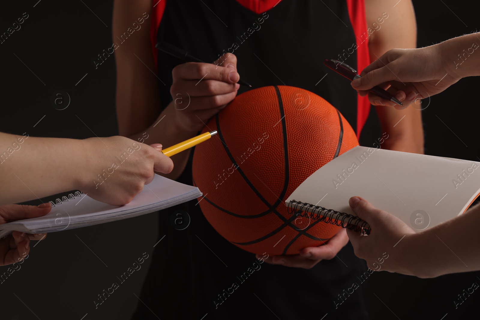 Photo of Sportsman signing autograph on basketball ball against black background, closeup