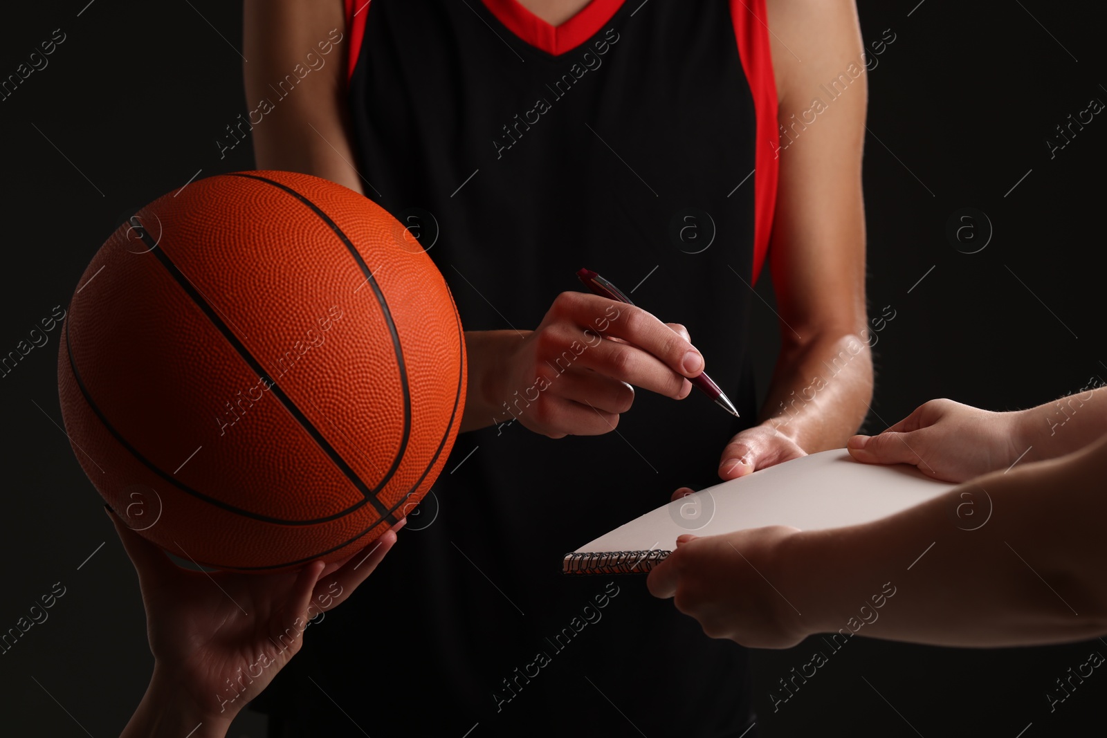 Photo of Sportsman signing autograph in notebook on black background, closeup