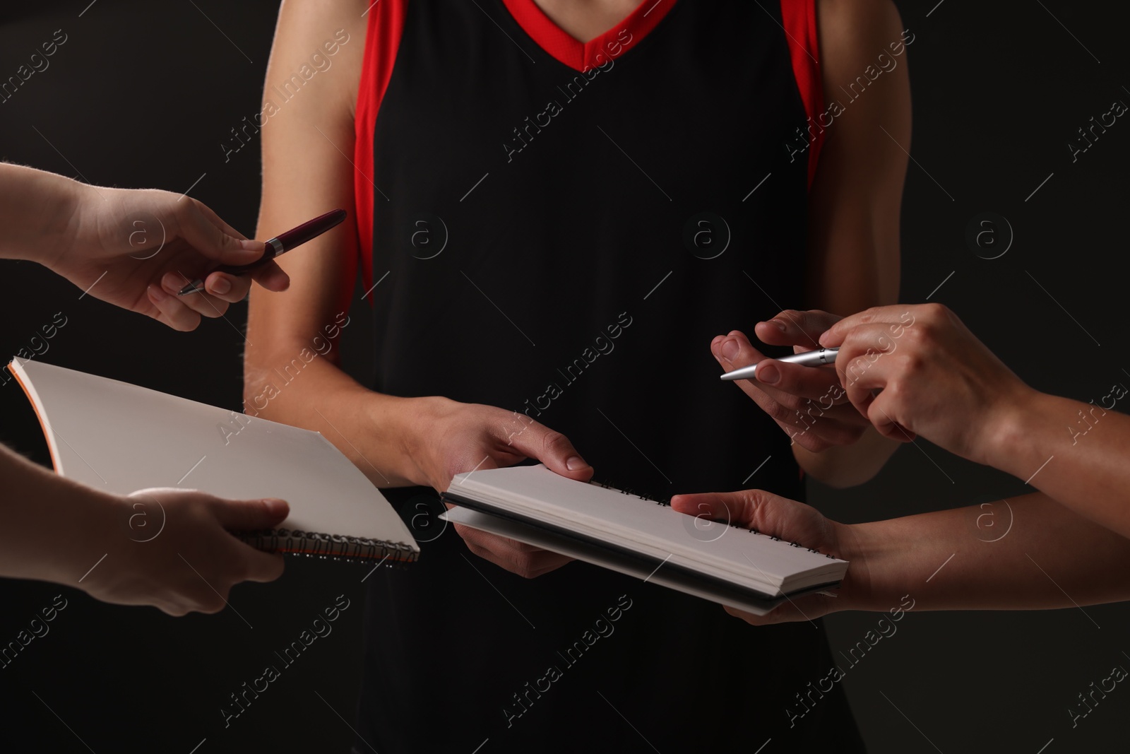 Photo of Sportsman signing autograph in notebooks on black background, closeup