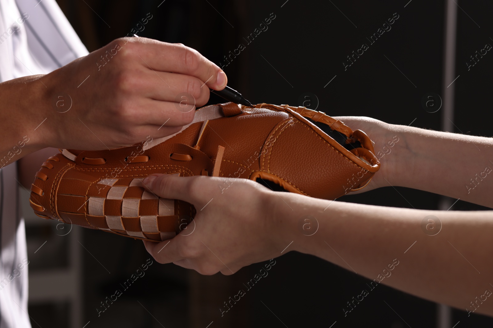 Photo of Baseball player signing autograph on leather glove against black background, closeup