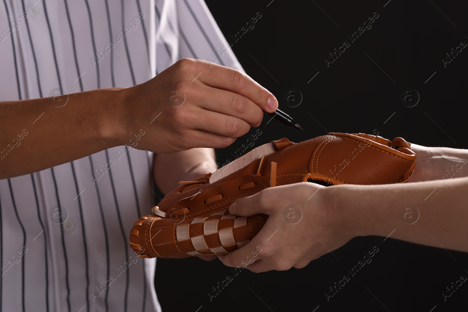 Photo of Baseball player signing autograph on leather glove against black background, closeup