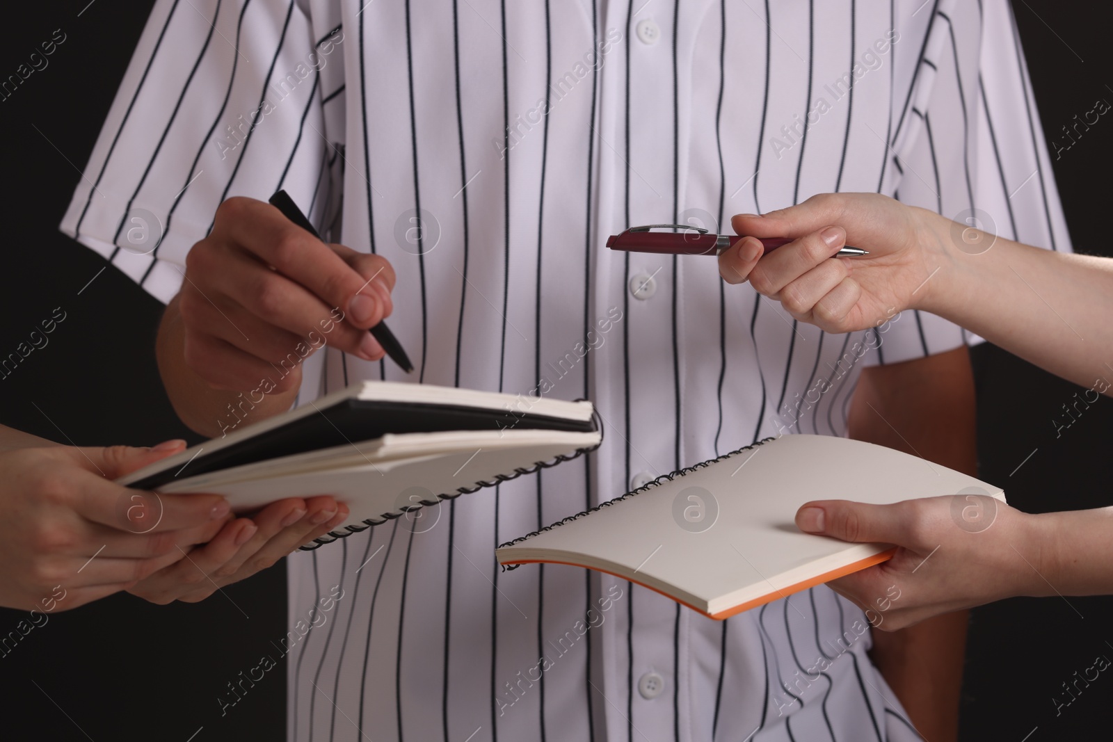 Photo of Baseball player signing autograph in notebook against black background, closeup