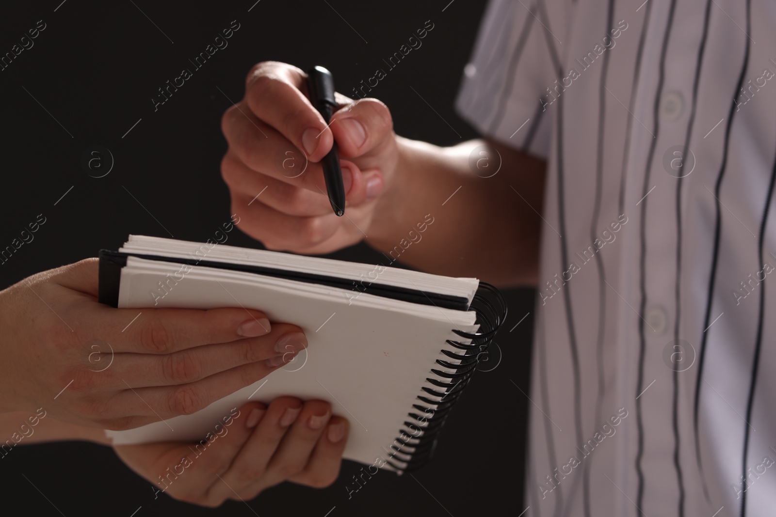 Photo of Baseball player signing autograph in notebook against black background, closeup