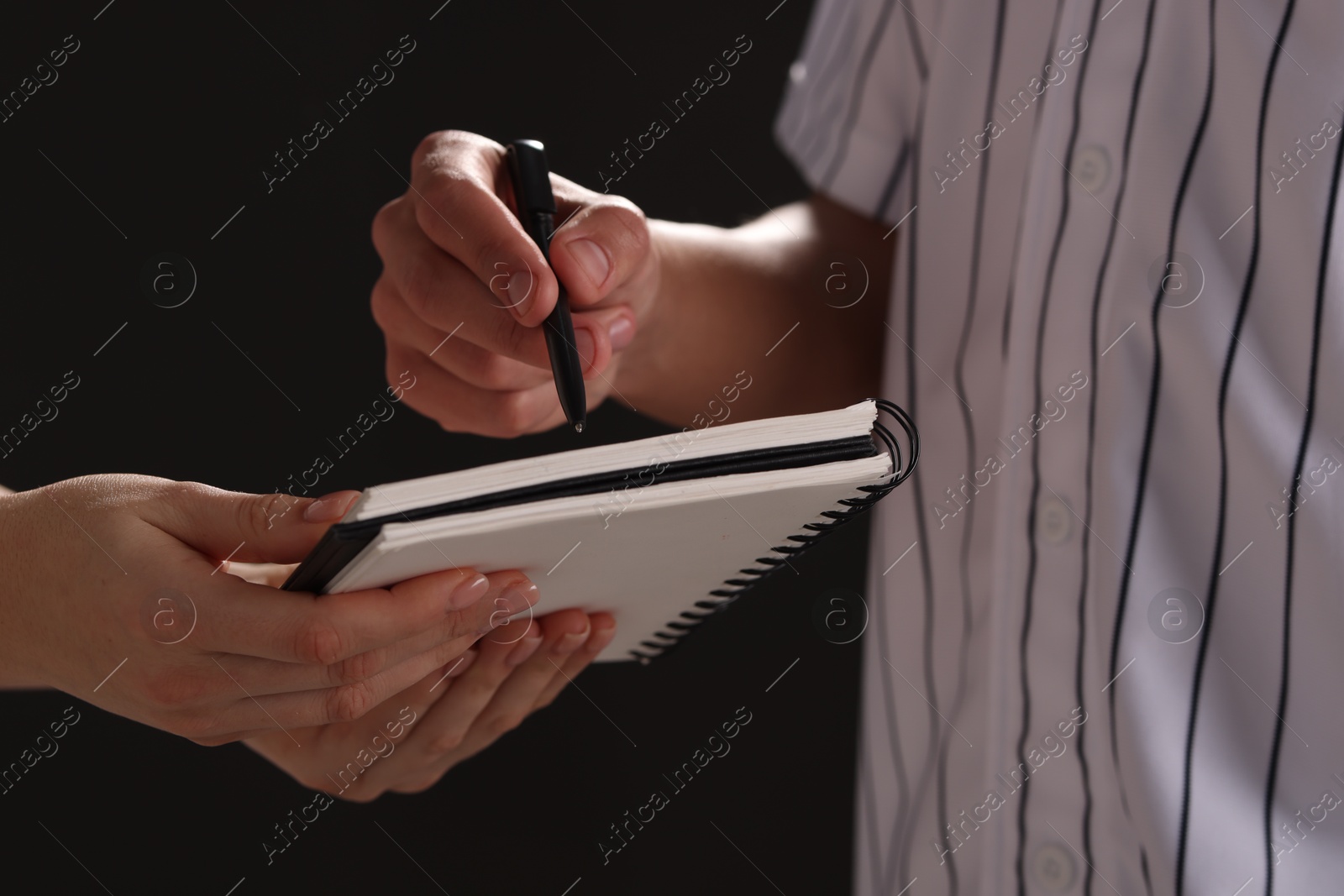 Photo of Baseball player signing autograph in notebook against black background, closeup