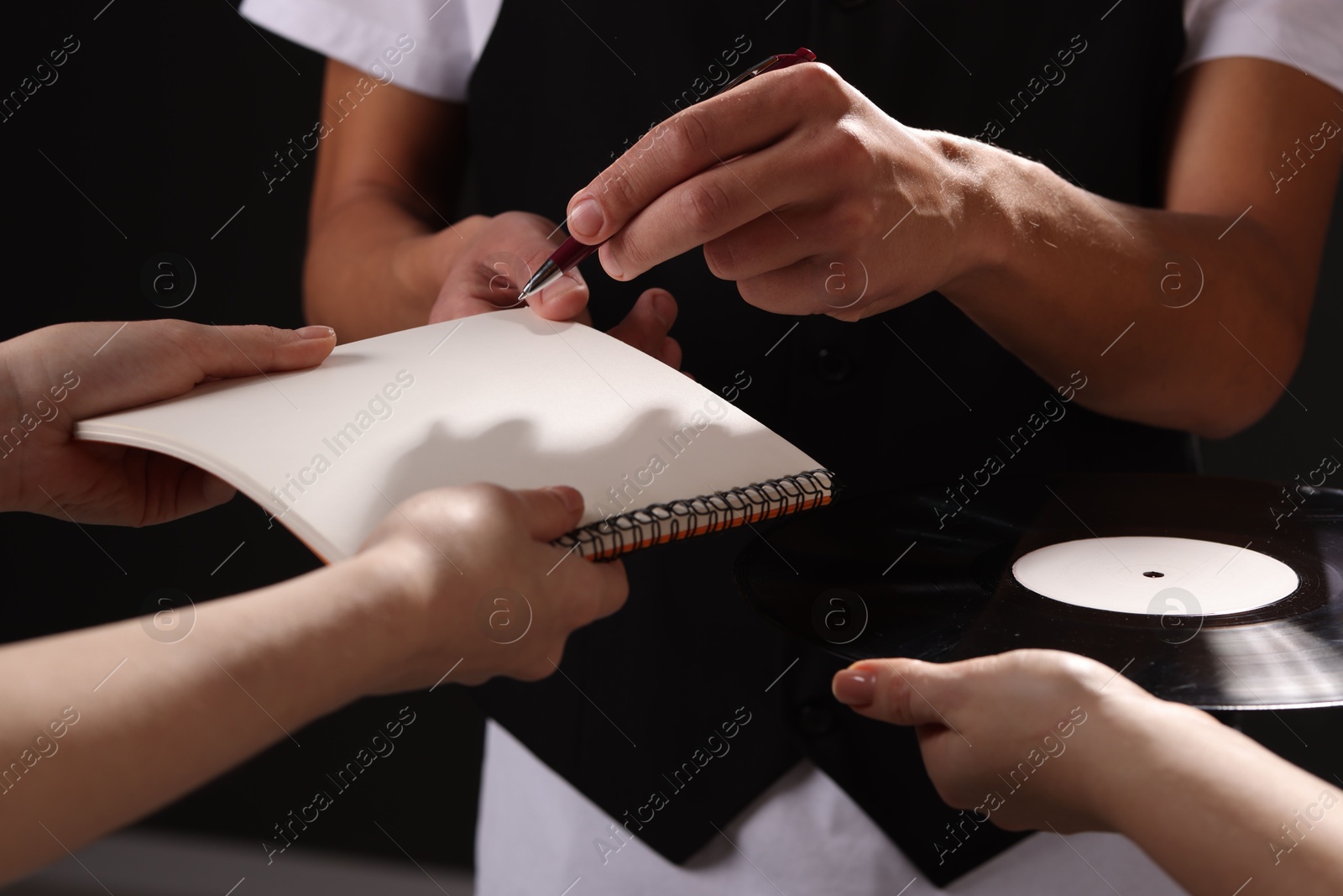 Photo of Singer signing autograph in notebook on dark background, closeup